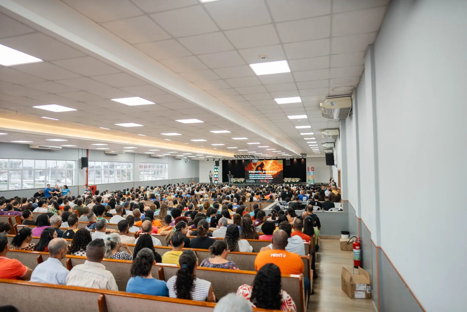 Grande salle plénière avec 300 chaises face à une scène éclairée, vue depuis le fond de la salle